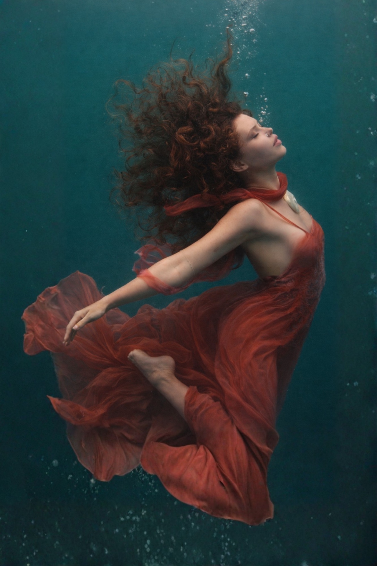 Moonessa, singer and songwriter, floating underwater in a flowing red gown — official press photo.